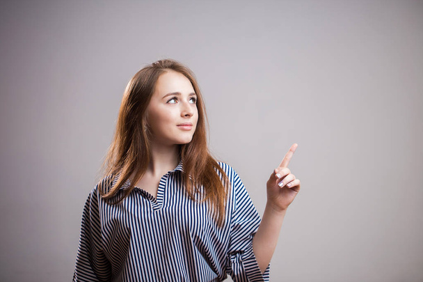 Beautiful young redhead woman pointing finger at copy space for text on grey background. Advertising, presentation of a new product, banner - Φωτογραφία, εικόνα
