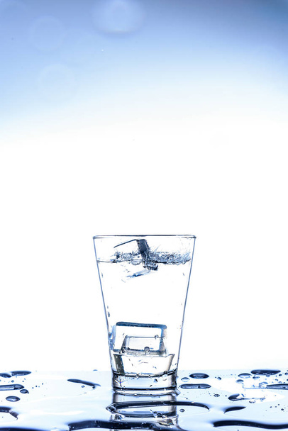 Eistropfen und Wasserspritzer im Glas mit Reflexion auf dem Spiegeltisch und isoliert auf weißem Hintergrund. - Foto, Bild