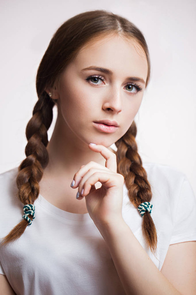 Close up portrait of sensual beautiful young girl on white background. Attractive woman with long eyelashes and clean skin, braids wears a white t-shirt - Photo, Image