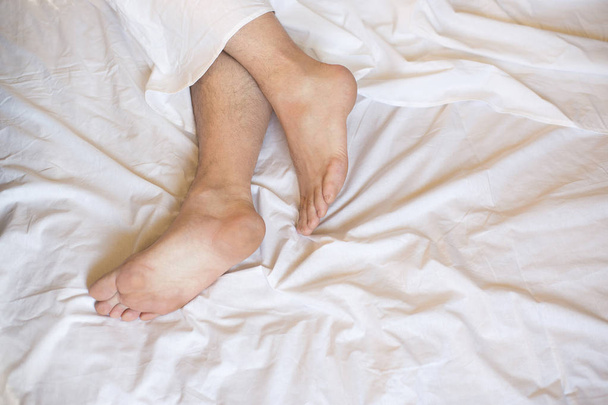 Male bare feet in a bed on white linen, selected focus - 写真・画像