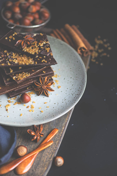 Ciemne kawałki czekolady zgnieciony na ciemny drewniany stół, przyprawy jak cynamon i anyżu star jako koncept gastronomiczny z kopia przestrzeń, widok z góry - Zdjęcie, obraz