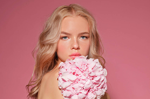 beautiful blonde model with nude makeup and flowers on pink background , close-up - Photo, image