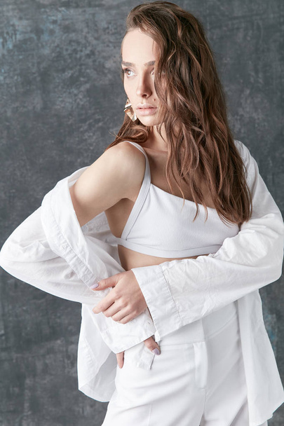 Sexy brunette female model posing in white shirt, top and pants. Studio shot, grey background  - Fotografie, Obrázek