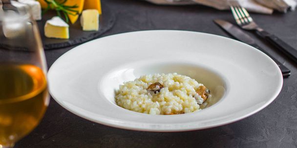 risottowith małże (ryż owoce) w biały talerz i kieliszek białego wineon ciemnym tle - Zdjęcie, obraz