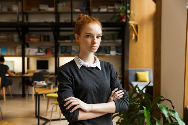 Image of beautiful serious concentrated redhead lady student posing indoors in library. - Foto, immagini
