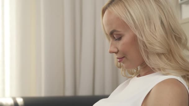 A side view portrait of a pregnant woman sitting on the sofa and caressing her belly. The camera moves top down - Záběry, video