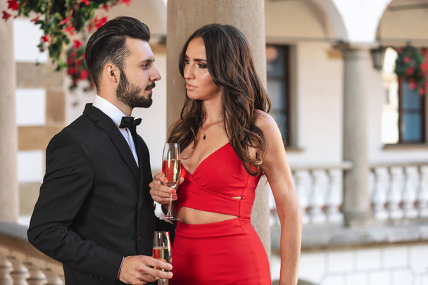 Elegante pareja de amantes con una copa de vino o champán en un balcón durante la fiesta de lujo
. - Foto, Imagen