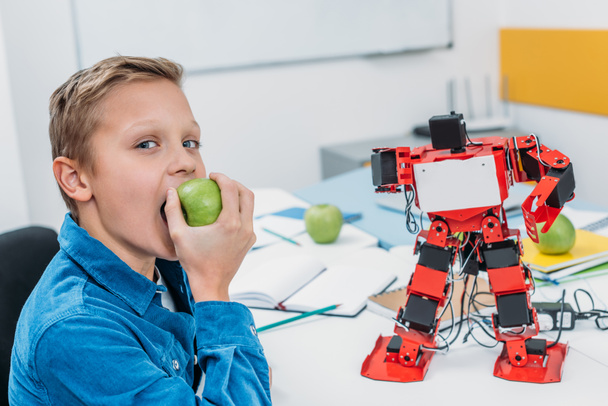 niño alegre comiendo manzana después de la lección de robótica STEM
  - Foto, Imagen