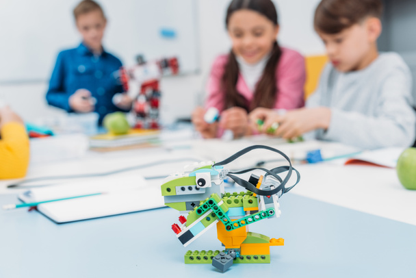 veelkleurige handgemaakte robot aan balie met schoolkinderen op de achtergrond in de klasse van de stam - Foto, afbeelding