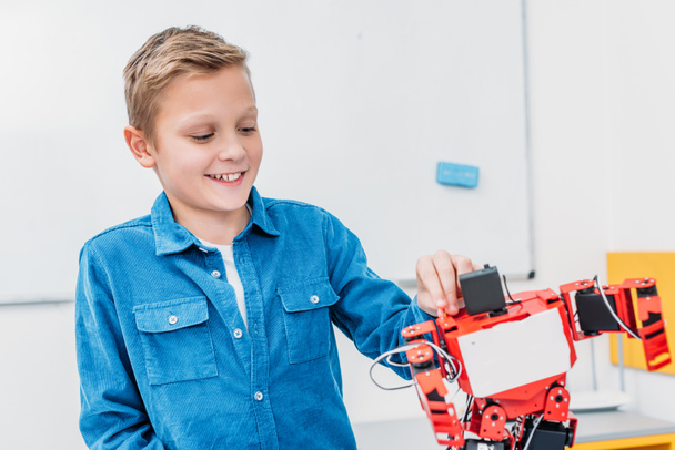 smiling schoolboy touching red robot in stem class - Foto, Imagem