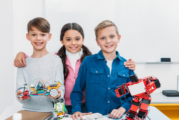счастливые школьники, держащие электрического робота и глядя на камеру в стебельном классе
 - Фото, изображение