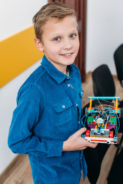 smiling schoolboy standing, looking at camera and holding handmade robot in stem class - Fotoğraf, Görsel
