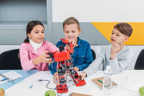 Улыбающиеся школьники строят красный электрический робот во время урока STEM
 - Фото, изображение