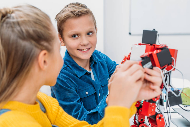 Schüler und Schülerin schauen einander an und berühren handgefertigten Roboter im Unterricht - Foto, Bild