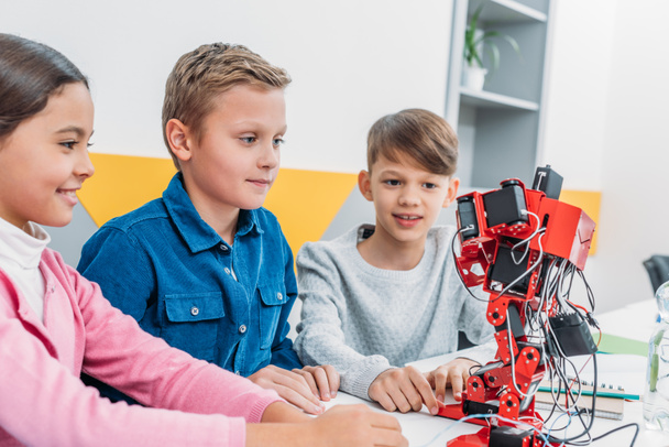 Улыбающиеся школьники смотрят на красного пластикового робота в классе
 - Фото, изображение