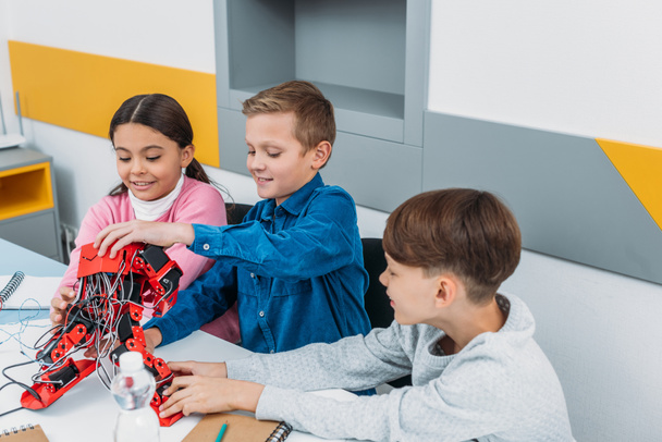 улыбающиеся школьники касаются красного электрического робота на рабочем столе в классе
 - Фото, изображение