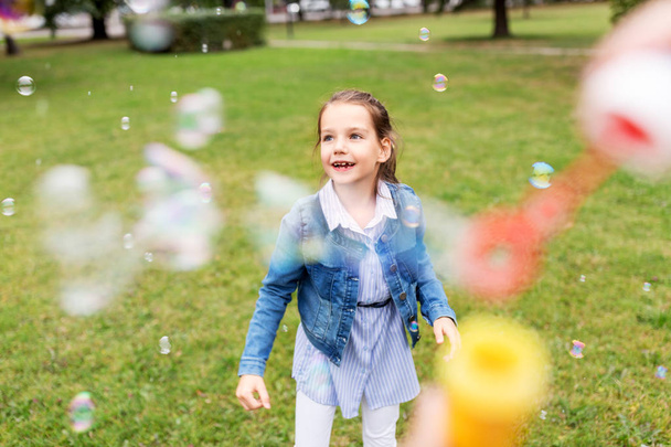 happy girl playing with soap bubbles at park - Fotó, kép