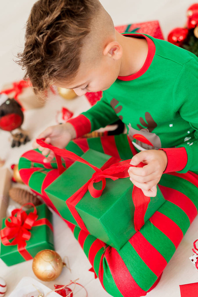 Curious young boy wearing xmas pajamas sitting on the floor, opening his christmas present, top view. - Photo, Image