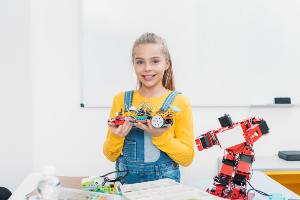 Lächelndes Schulmädchen blickt in die Kamera und präsentiert handgemachtes Robotermodell bei Stammlektion - Foto, Bild