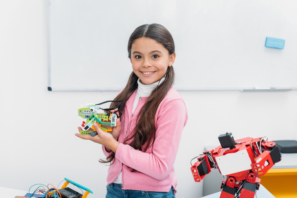 colegiala sonriente mirando a la cámara y presentando el modelo de robot hecho a mano en la lección STEM
 - Foto, imagen
