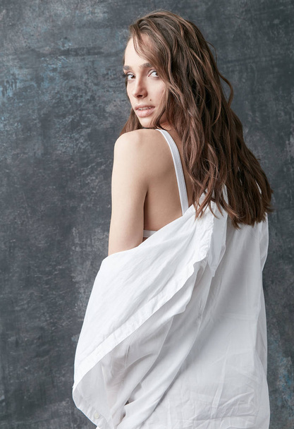Fashion shot of beautiful brunette woman posing in white shirt, top and pants. Studio, grey background - Fotó, kép