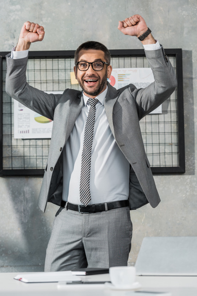 cheerful businessman triumphing and smiling at camera in office - Foto, afbeelding