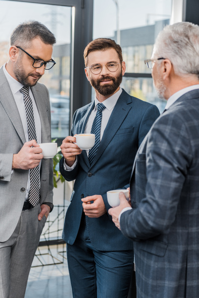 businessmen holding cups of coffee and talking in office - Foto, Bild