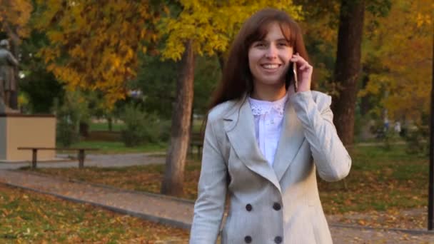 όμορφη γυναίκα, μιλώντας σε κινητό τηλέφωνο, ευτυχισμένος κορίτσι περπατώντας το φθινόπωρο στο πάρκο και χαμογελαστός - Πλάνα, βίντεο