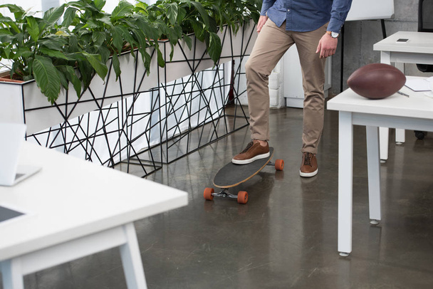 low section of businessman standing on skateboard in office - Photo, Image