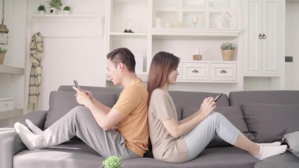アジアのカップルは、自宅のリビング ルームでスマート フォン チェック ソーシャル メディアを使用して、甘いカップルは、ソファの上に横たわっている間愛の瞬間を楽しむ家でくつろぐとき。ライフ スタイルのカップルは家でくつろぐコンセプト. - 映像、動画
