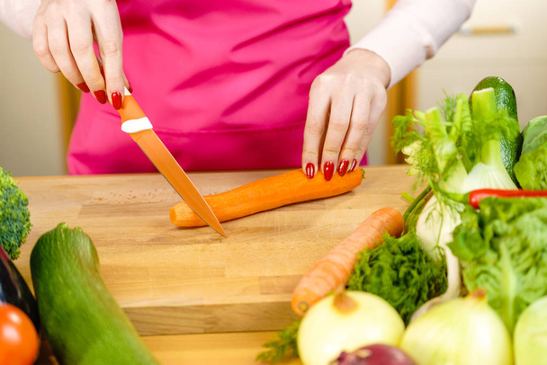 Woman cutting, preparing vegetable, delicious sweet carrot using kitchen knife. Female hands making food. - Foto, afbeelding