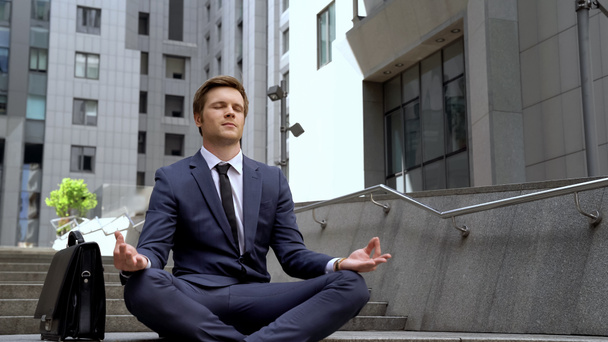 Hombre guapo sentado en posición de loto cerca del moderno centro de oficina, calma
 - Foto, Imagen