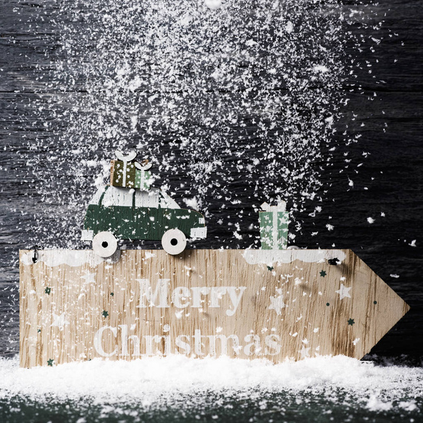 un letrero de madera hecho en forma de flecha con el texto feliz navidad escrita en, contra una superficie de madera rústica gris, cubierto por la nieve
 - Foto, imagen