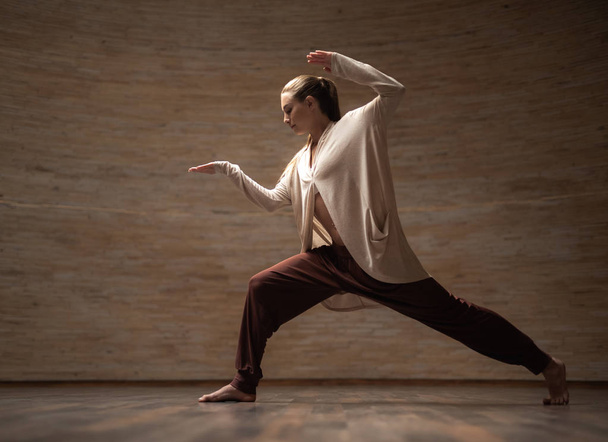 Slim lady putting hands up and finding balance while having chi gong training - 写真・画像