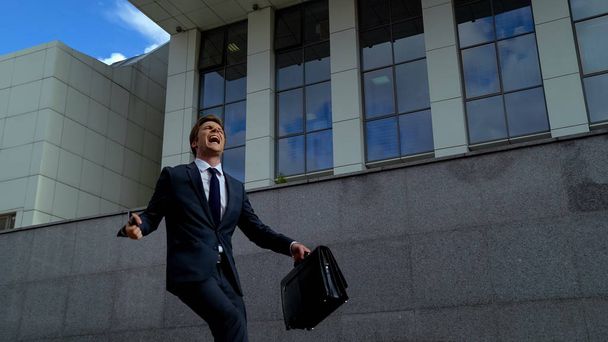 Very happy office worker getting promotion, dancing outdoors near office center - 写真・画像