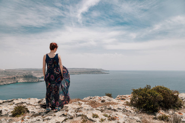 Young redhead woman in long dress moving with wind standing on edge of cliff  - Fotografie, Obrázek
