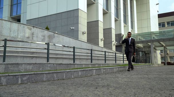 Mulatto businessman talking on phone near office building, successful career - Фото, зображення