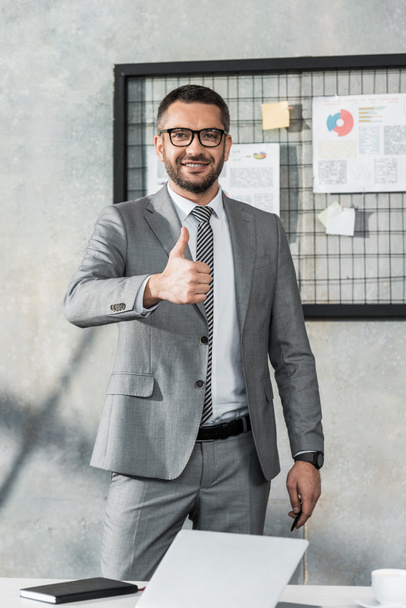 handsome businessman showing thumb up and looking at camera in office - Фото, зображення