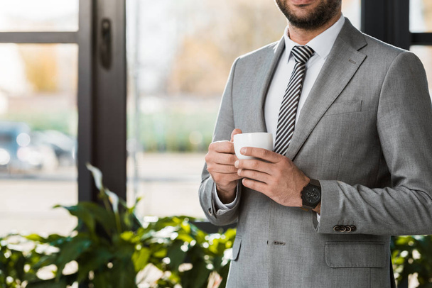 cropped image of businessman holding cup of coffee in office - Fotoğraf, Görsel