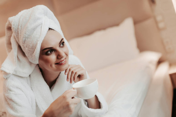 Young woman in bathrobe lying on bed with tea - Foto, Imagem
