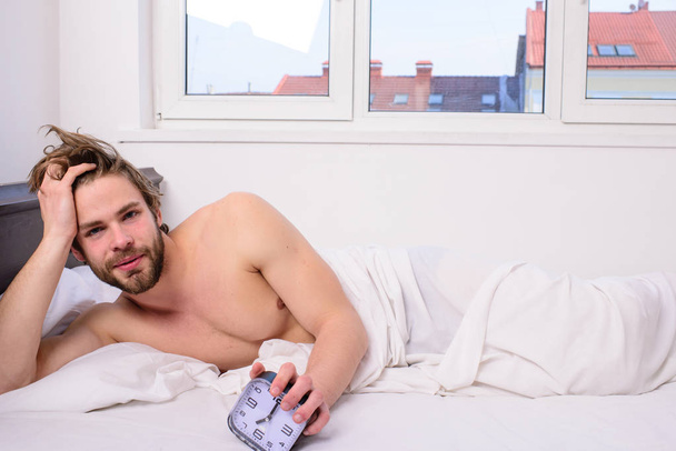 Man unshaven lay bed hold alarm clock. Man unshaven bearded wakeful face having rest. Stick schedule same bedtime wake up time. Enough sleep for him. Regulate your bodys clock. Sleep regime habit - Фото, зображення