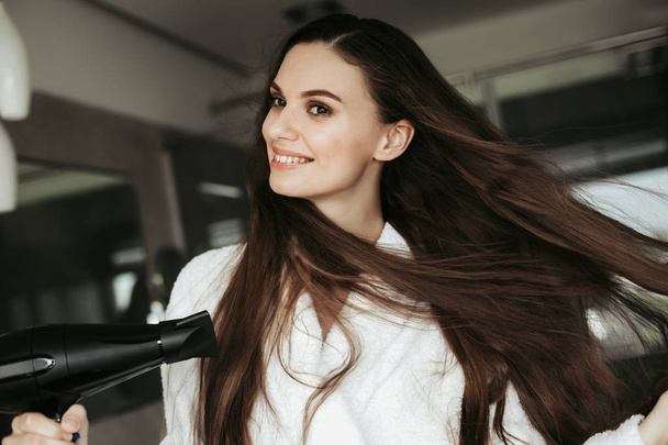 Young cheerful female drying hair with blowdryer - Foto, Bild