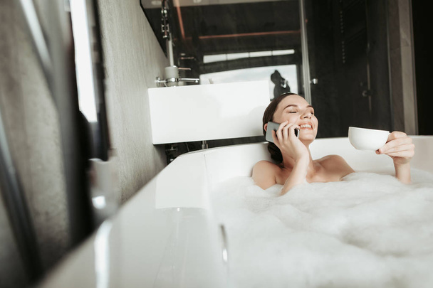 Young woman talking by phone while taking bath - Zdjęcie, obraz