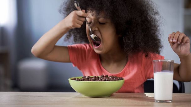 Cute black-haired curly girl eating chocolate cornflakes, unhealthy sugary food - Fotoğraf, Görsel