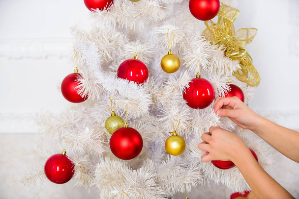 Hands of child put christmas ornament ball on artificial white tree. Christmas decoration concept. Eco movement and artificial plastic christmas tree. Winter holiday decor. Bright christmas decor - Foto, imagen