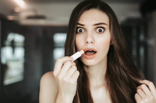 Bemused woman holding lipstick in arm indoor - Fotografie, Obrázek