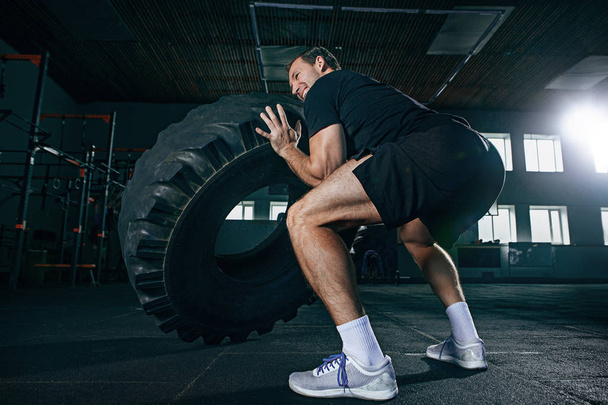 Shirtless man flipping heavy tire at gym - Fotó, kép