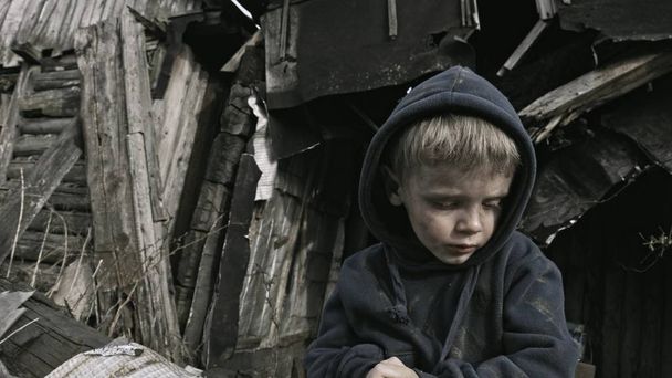 portrait of homeless orphan boy sitting and crying beside abandoned building - Fotó, kép