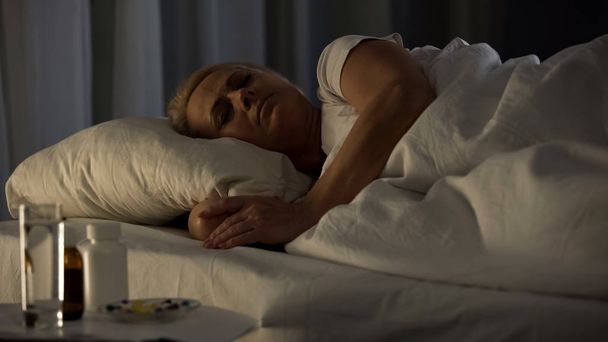 Μεσήλικη κυρία στον ύπνο στο κρεβάτι, πίνακα χάπια θεραπεία, περίθαλψη, ιατρική - Φωτογραφία, εικόνα