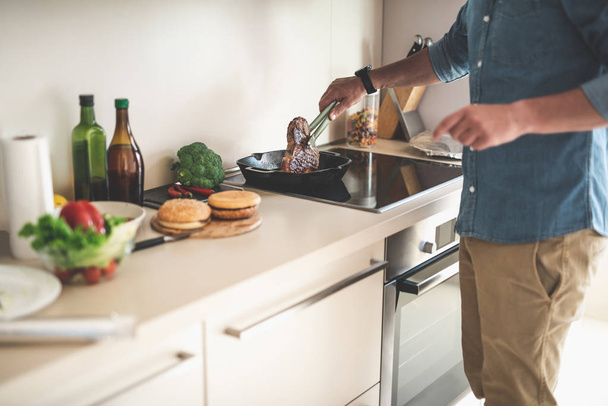 Man in denim shirt cooking meat in kitchen at home - Foto, Bild